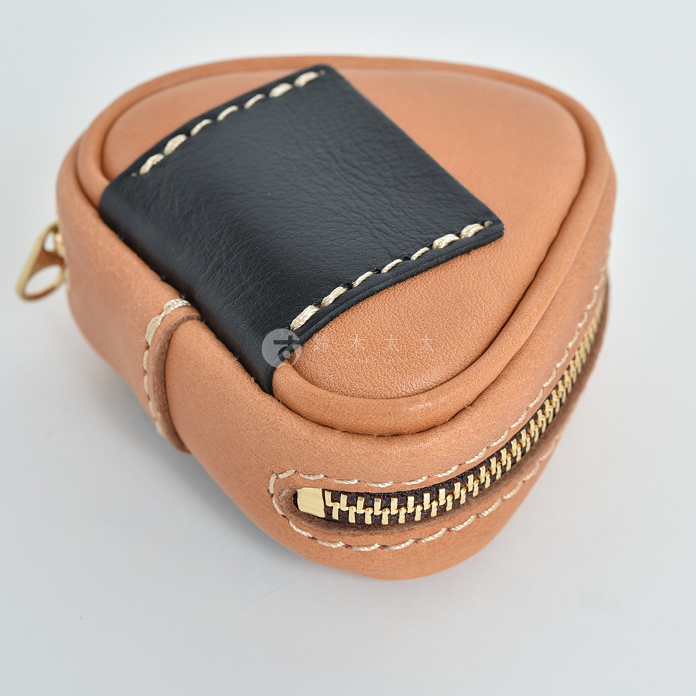 棕色皮革製成的三角飯糰造型小物收納包，上方飾有黑色皮革拼貼，以白色縫線勾勒出邊緣，側邊配有金色拉鍊，整體呈現精緻手作質感。