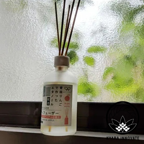 日式香氛瓶，玻璃瓶身裝有擴香枝，背景是模糊的綠色樹葉和玻璃窗。