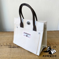 犬印純棉帆布迷你托特包，米白色帆布材質，配有深棕色提把。包包正面有一個大口袋，上面貼有帶有日文圖案的標籤，並有金屬鈕扣固定。