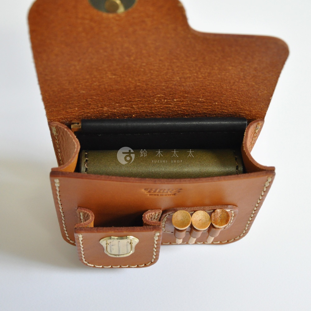 職人手作皮革高爾夫腰包，主體為棕褐色光滑皮革，內有黑色襯裡，綠色物品置於其中。腰包前方有小隔層，配有金屬扣，並有三個木質高爾夫球釘插槽。