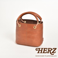 棕色皮革製成的圓筒形午餐袋，配有加厚提把，袋口有銅環及束繩設計，整體採用職人手作縫線工藝。