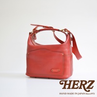 紅色厚實皮革單肩波士頓包，配有拉鍊開合、前袋、側袋及可調節肩帶，黃銅五金配件，手工縫製。