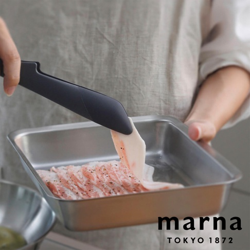 MARNA TOKYO 1872 品牌的可拆解式食物夾正在夾取一塊淋上調味料的生豬肉，準備放入金屬烤盤中。