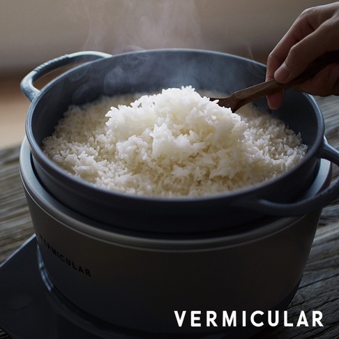 一個灰色的 Vermicular 鑄鐵電子鍋，鍋內裝滿了熱騰騰的米飯，一隻手正用木勺舀取米飯。