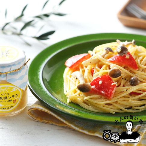 一盤義大利麵，麵條呈淡黃色，配有切塊的番茄、蘑菇和醬汁。旁邊是一個標有「熟成藻鹽漬檸檬」的玻璃罐，罐身上有藍白相間的波浪紋和太陽圖案。