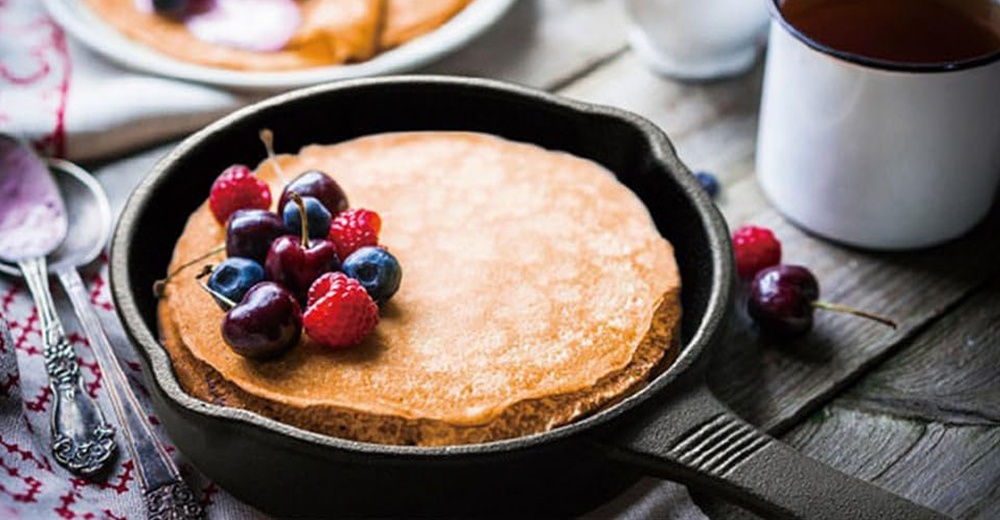 黑色鑄鐵平底鍋盛有堆疊的薄餅，頂部裝飾著新鮮的藍莓、覆盆子和櫻桃。