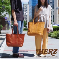 兩位模特兒手持職人手作皮革經典托特包，左側為棕褐色皮革包，右側為黃褐色皮革包，皆為簡約設計，適合日常搭配。