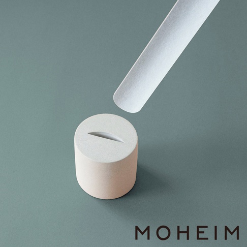 淺米色圓柱形鞋拔座，上方有一個斜切槽口，搭配一支白色長柄鞋拔，置於灰綠色背景上。