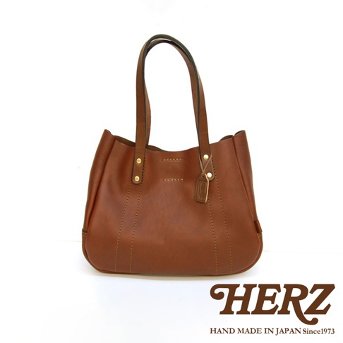 職人手作皮革仕女托特包 T-10，呈現經典的咖啡棕色，採用柔軟的真皮材質，搭配穩固的雙提把設計，包身線條流暢，縫線精緻，底部圓潤，整體風格簡約大方。