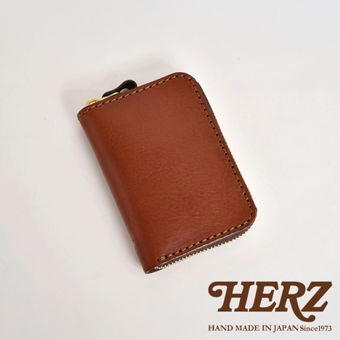 職人手作棕色皮革多用途收納鑰匙包，以精緻縫線勾勒邊緣，配有金色拉鍊，展示品牌「HERZ」標誌及「HAND MADE IN JAPAN Since1973」字樣。
