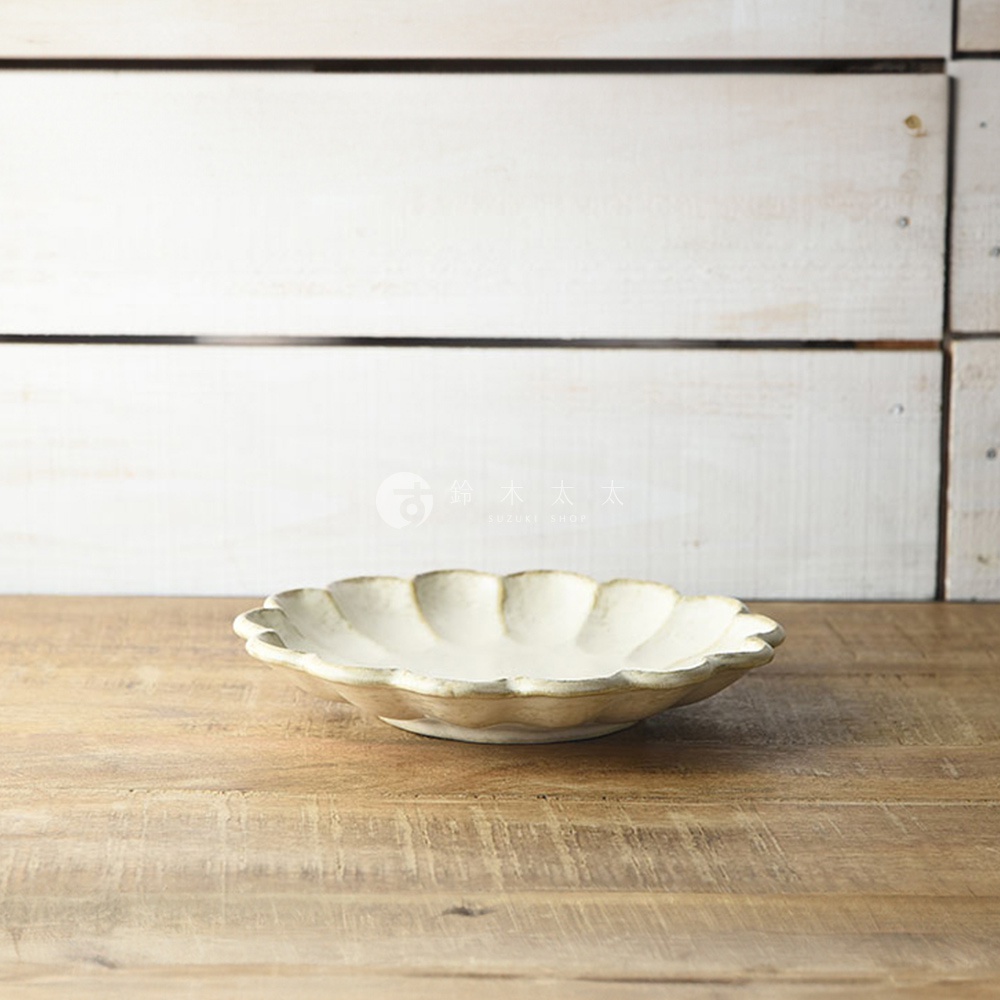 一個淺色的、帶有花瓣狀邊緣的陶瓷主食盤，盤面有自然的紋理，整體呈現樸實的風格。
