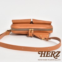 職人手作皮革雙口袋斜背包，採用棕色皮革製成，配有金色拉鍊和可調節的皮革背帶。包身設計簡潔，前方有兩個立體口袋，適合日常收納。