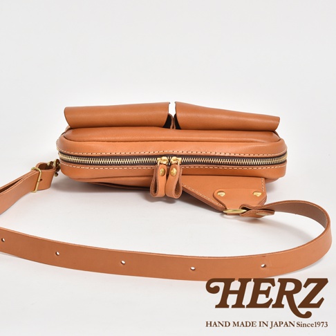 職人手作皮革雙口袋斜背包，採用棕色皮革製成，配有金色拉鍊和可調節的皮革背帶。包身設計簡潔，前方有兩個立體口袋，適合日常收納。