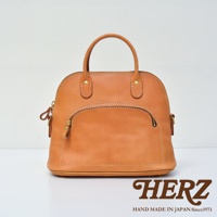 棕褐色皮革貝殼造型手提包，設有圓形提把、拉鍊開口及正面拉鍊口袋，精緻縫線裝飾，展現職人手作質感。