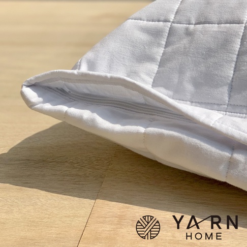 白色格紋枕套，採用脫脂棉混紗材質，帶有拉鍊開口，展示於木質表面。