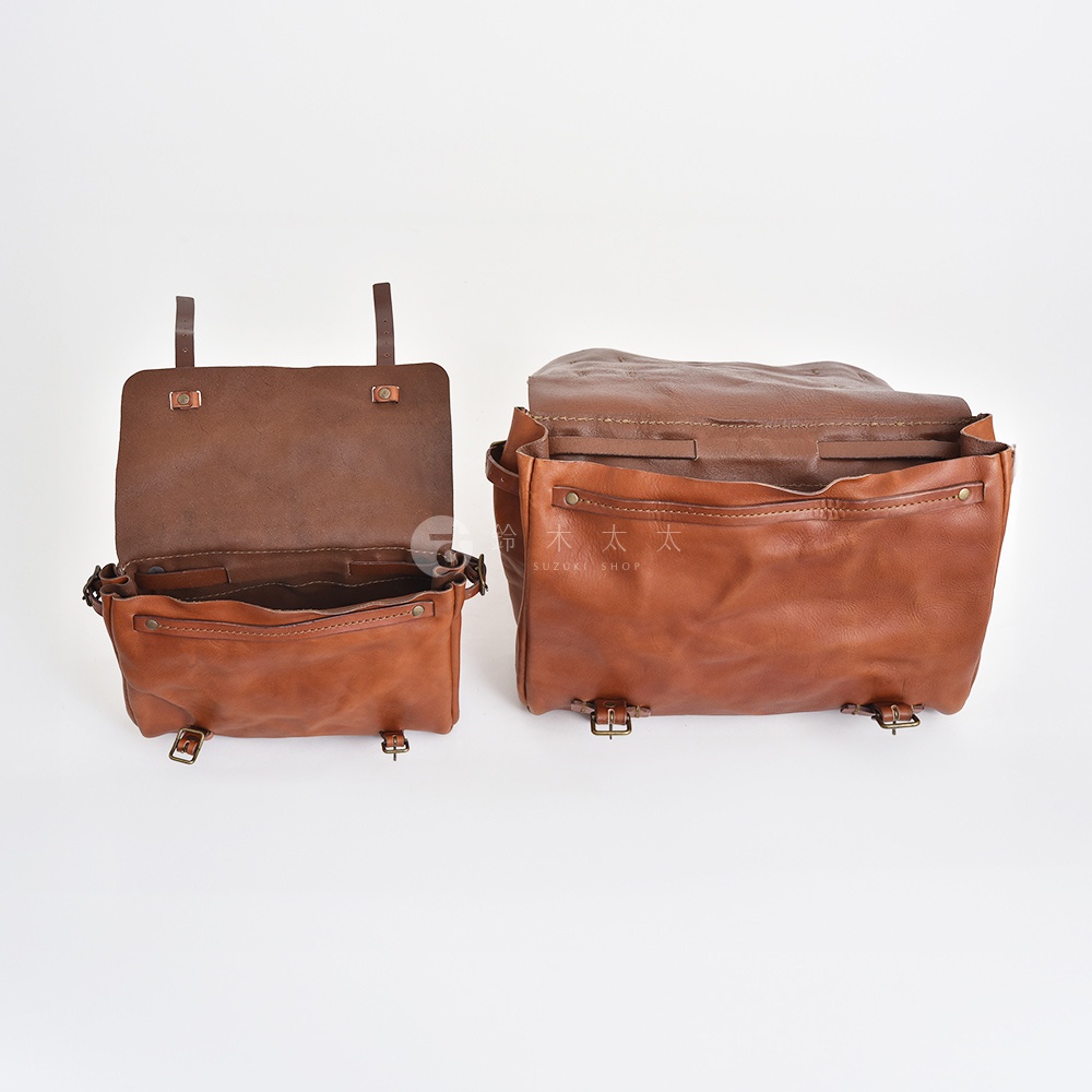 兩款棕色皮革復古郵差包，左側包款開蓋展示內裡，右側包款則為閉合狀態，兩款均配有金屬釦環與皮帶。