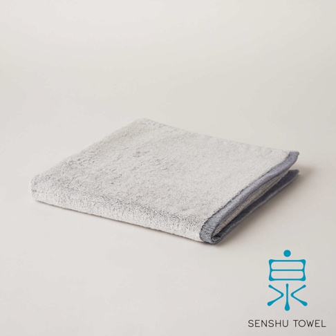 YUKINONE 雪之音柔織有機棉浴巾，淺灰色，觸感柔軟，邊緣有深藍色滾邊。