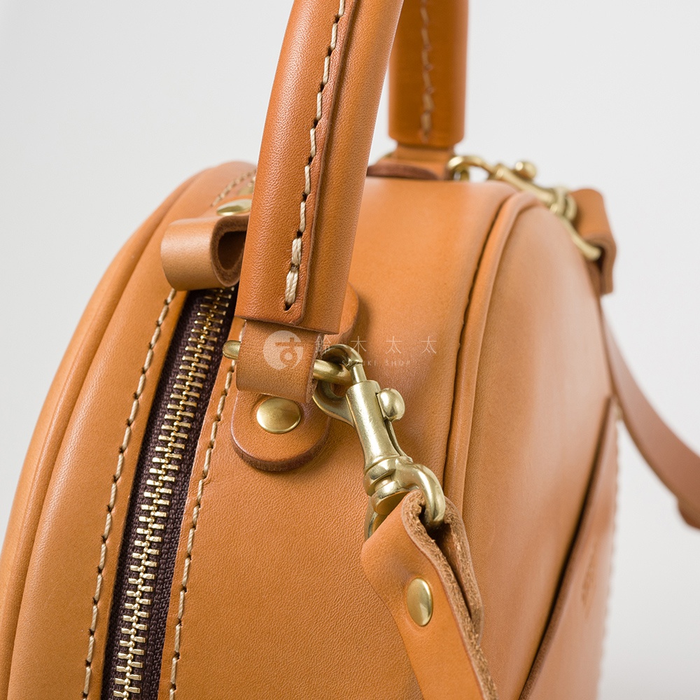 圓形棕色皮革手提包特寫，展示拉鍊、金色金屬配件和縫線細節