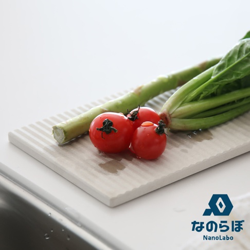 淺灰色長條形珪藻土吸水墊，表面有平行凹槽，上面放著三顆小番茄和一束綠色蔬菜。
