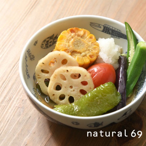 陶瓷碗中盛有切片蓮藕、玉米、番茄、茄子、青椒、秋葵和磨碎的蘿蔔，碗內有藍色魚形圖案。