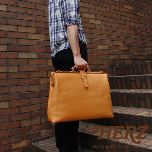 職人手作皮革軟式杜勒斯包，淺棕色皮革，方形包身，有頂部提把及金屬扣環，適合商務或旅行使用。