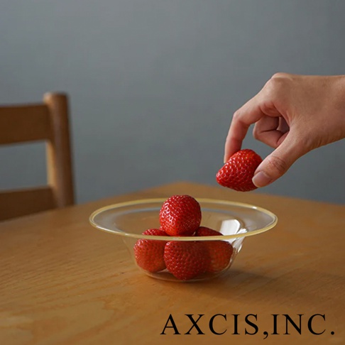 一個清透的玻璃深型點心碗，碗內盛有數顆新鮮草莓，一隻手正在將一顆草莓放入碗中。