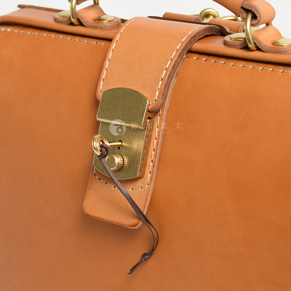淺棕色牛皮商務後背包，特寫鎖扣細節，金色金屬鎖具搭配皮革繫帶，縫線清晰，整體質感佳。
