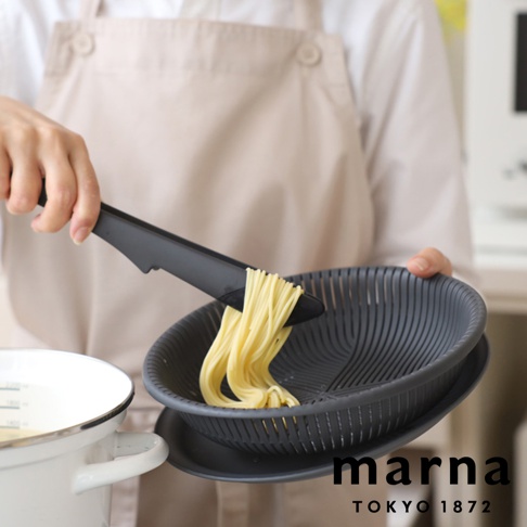 手持黑色夾子夾著煮好的義大利麵，準備放入同為黑色的濾網盆中，旁邊有一個白色的鍋子。