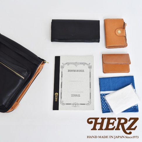 黑色皮革斜背包，搭配棕色皮夾、筆記本和藍色印花布。