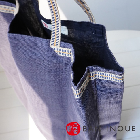 深藍色蚊帳棉織隨身購物袋，有米白色與金黃色交織的織帶裝飾提把與袋口邊緣，材質輕薄透氣。