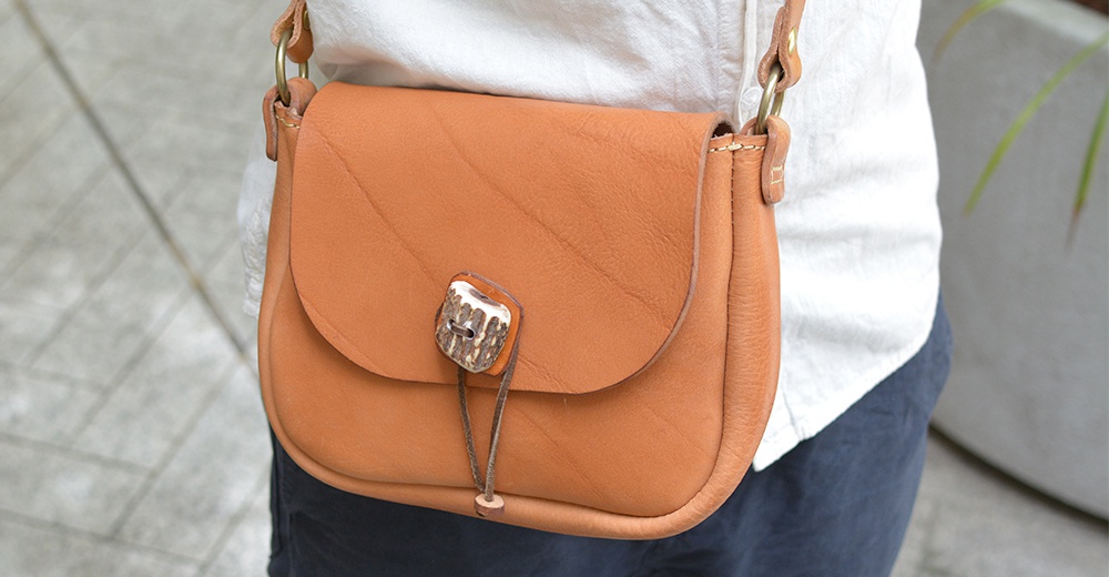 職人手作皮革鹿角扣繩肩背包，採用棕褐色皮革製成，包蓋上有獨特的鹿角鈕扣與繫繩設計，肩帶為皮革材質。