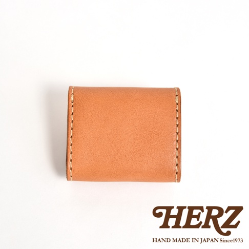 日本HERZ職人手作皮革零錢包，呈現暖棕色Stare皮革質感，採簡約雙折對稱設計，邊緣以細膩縫線加固，右下方標示品牌LOGO及手工產地資訊，整體呈現溫潤紮實的職人手作風格。
