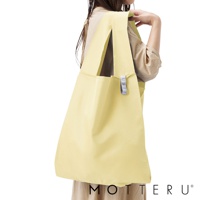 一位女性左肩上搭著一個淺黃色的大容量摺疊環保隨行袋，袋子為尼龍材質，附有同色系的提把，側面有一個灰色小標籤。