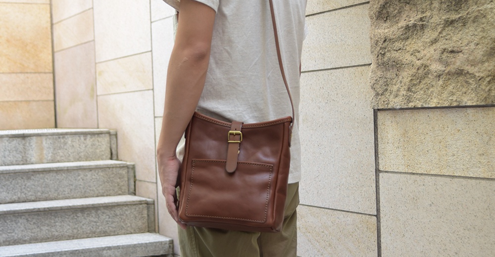 職人手作咖啡色皮革輕便單肩側背包，配有金屬釦帶和前方貼袋，適合日常攜帶。