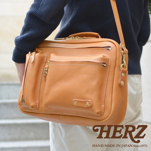 棕褐色皮革製成的多功能單肩包，具有多個拉鍊隔層和口袋，包身有明顯的縫線細節，並飾有品牌標誌。