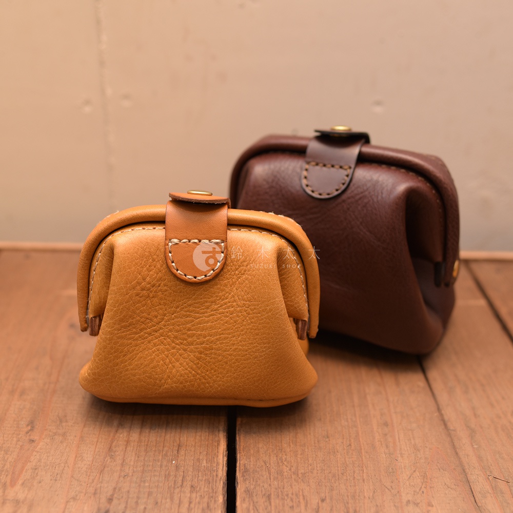 兩個職人手作皮革口金化妝包，一個為淺棕色，另一個為深棕色，皆採用天然皮革，帶有金屬開口和手工縫線細節。