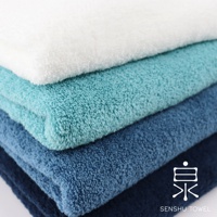堆疊的浴巾，由上至下顏色由白、淺藍綠、藍綠、深藍構成，材質為柔軟長纖維。