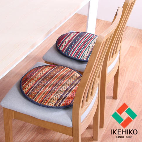 兩張天然藺草紋織圓型坐墊，分別呈現條紋狀的紅藍綠色調與紅棕色調，坐墊邊緣為深藍色布邊，置於淺灰色布面的木質餐椅上。