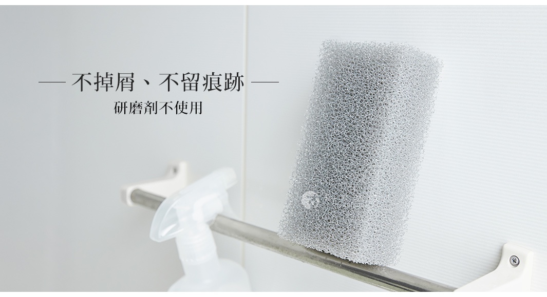 灰色多孔材質的浴室清潔海綿，置於金屬掛桿上，旁邊有一個白色噴霧瓶。