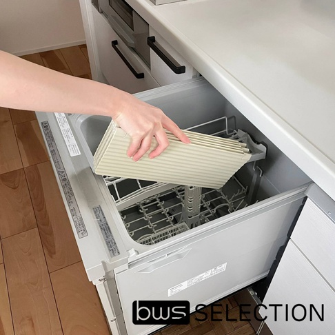 一隻手正將淺米色、帶有細條紋的六片式摺疊隔板放入廚房洗碗機的抽屜內，隔板材質看似塑膠或金屬。