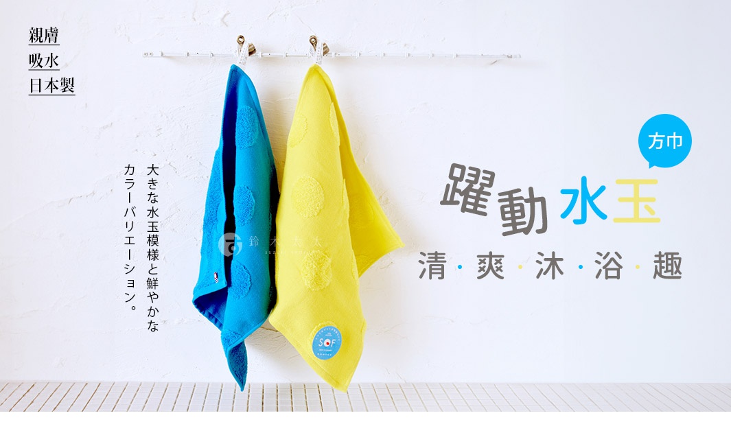 兩條懸掛在白色牆面掛桿上的純棉方巾，左側為鮮豔的藍色，右側為明亮的黃色，兩條方巾表面皆有立體的圓形點點紋路，黃色方巾下角貼有圓形藍色標籤，整體畫面呈現簡約日系風格，強調親膚吸水與日本製造的品質。