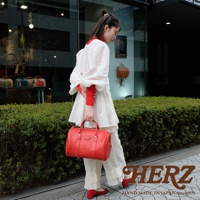 一名女子手提一個紅色皮革波士頓包，包包有拉鍊封口、雙提把，以及可拆卸肩帶。