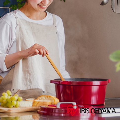 紅色萬用無水調理鍋24cm，鍋身光滑，帶有兩個鍋耳，鍋蓋上有提把，旁邊擺放著葡萄、麵包和起司。