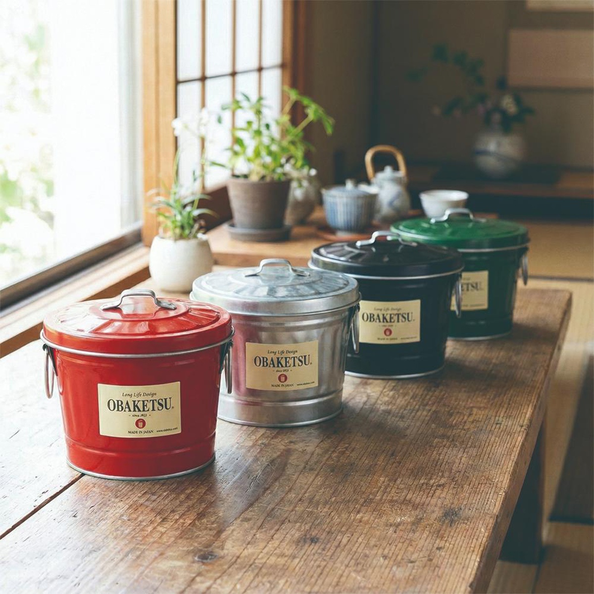 四個OBAKETSU品牌手工迷你儲物桶，分別為紅色、銀色、黑色和綠色，擺放在木桌上。