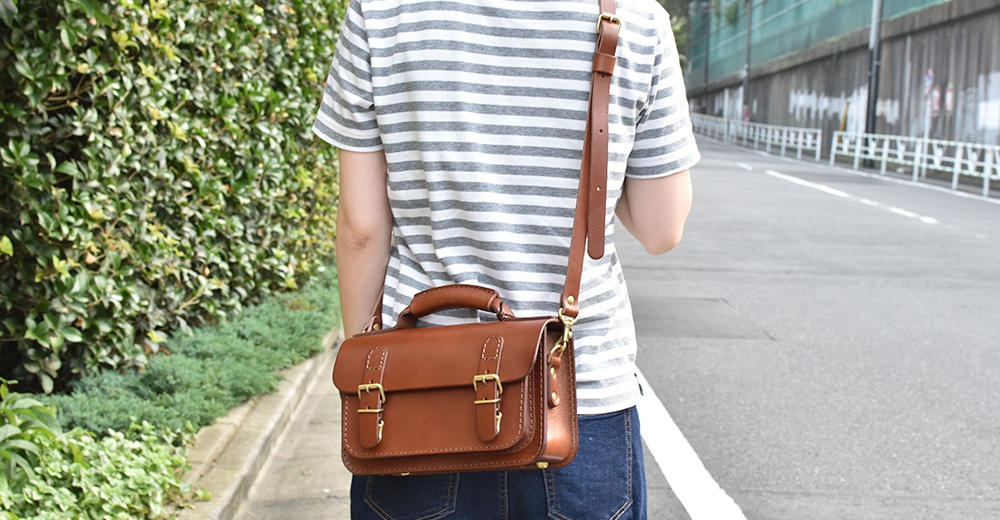 棕色皮革雙扣兩用迷你肩背包，配有提把及可拆卸肩帶，整體呈現復古風格。