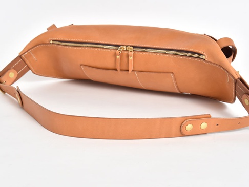 淺棕色皮革製成的大容量斜背包，帶有黃銅色拉鍊和铆釘，以及可調節的皮革肩帶。