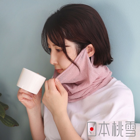 一位短髮女性側臉看向左方，手中拿著白色杯子，脖子上圍著一條粉紅色的日本桃雪絲綢護喉晚安半面罩，材質透薄親膚，不僅能保護頸部也兼具遮擋口鼻的功能，展現居家舒適的休閒風格。