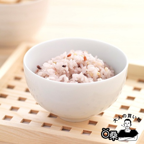 白色陶瓷碗中盛有混合了多種穀物的米飯，米粒呈淡粉色，混有少許深色穀物。碗放置在木質餐盤上。