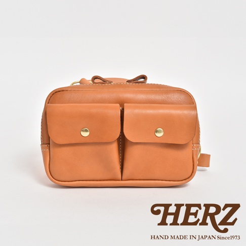 職人手作皮革雙口袋斜背包，淺棕色皮革材質，包身正面有兩個帶有金色金屬釦的翻蓋口袋，整體風格簡約實用。