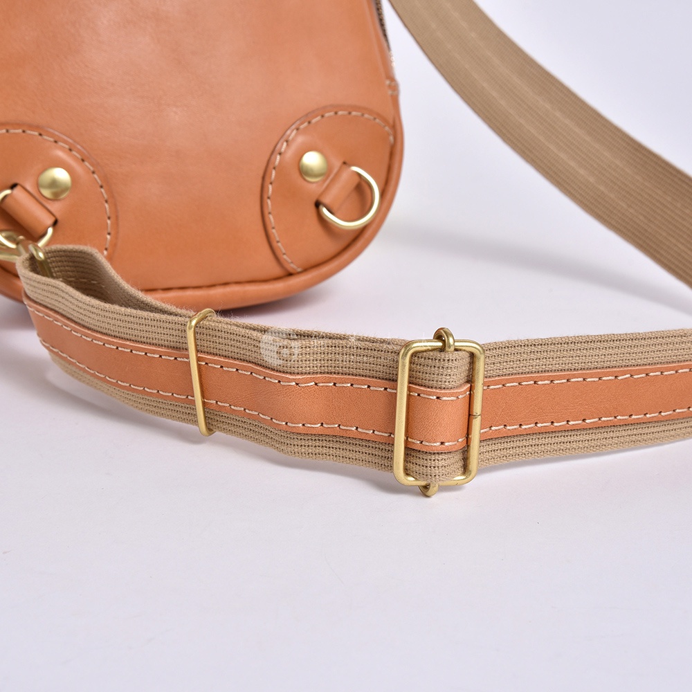 復古棕色皮革斜背包的棕色織帶和金色金屬帶扣特寫